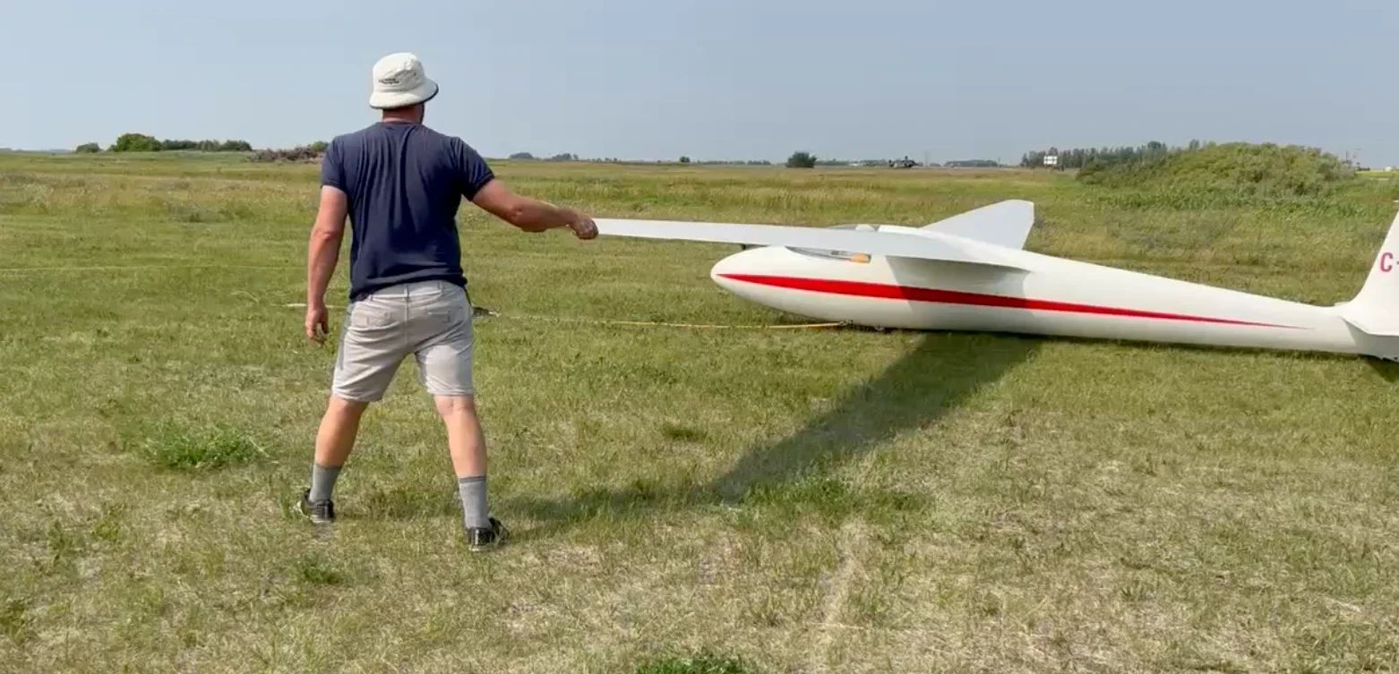 A club member holds a glider's wingtip level on the grass field, ready for launch